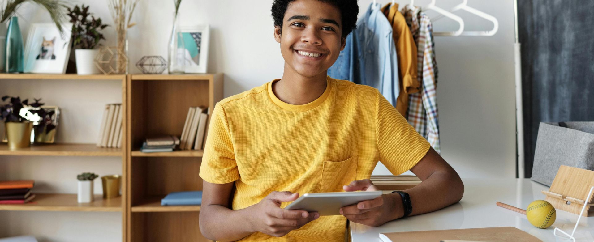 Smiling teenager using a tablet at his desk for online learning at home.